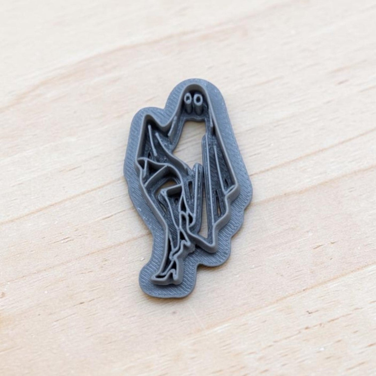 A small gray ghost-shaped cookie cutter or stamp with a spooky face, resting on a light-colored wooden surface.