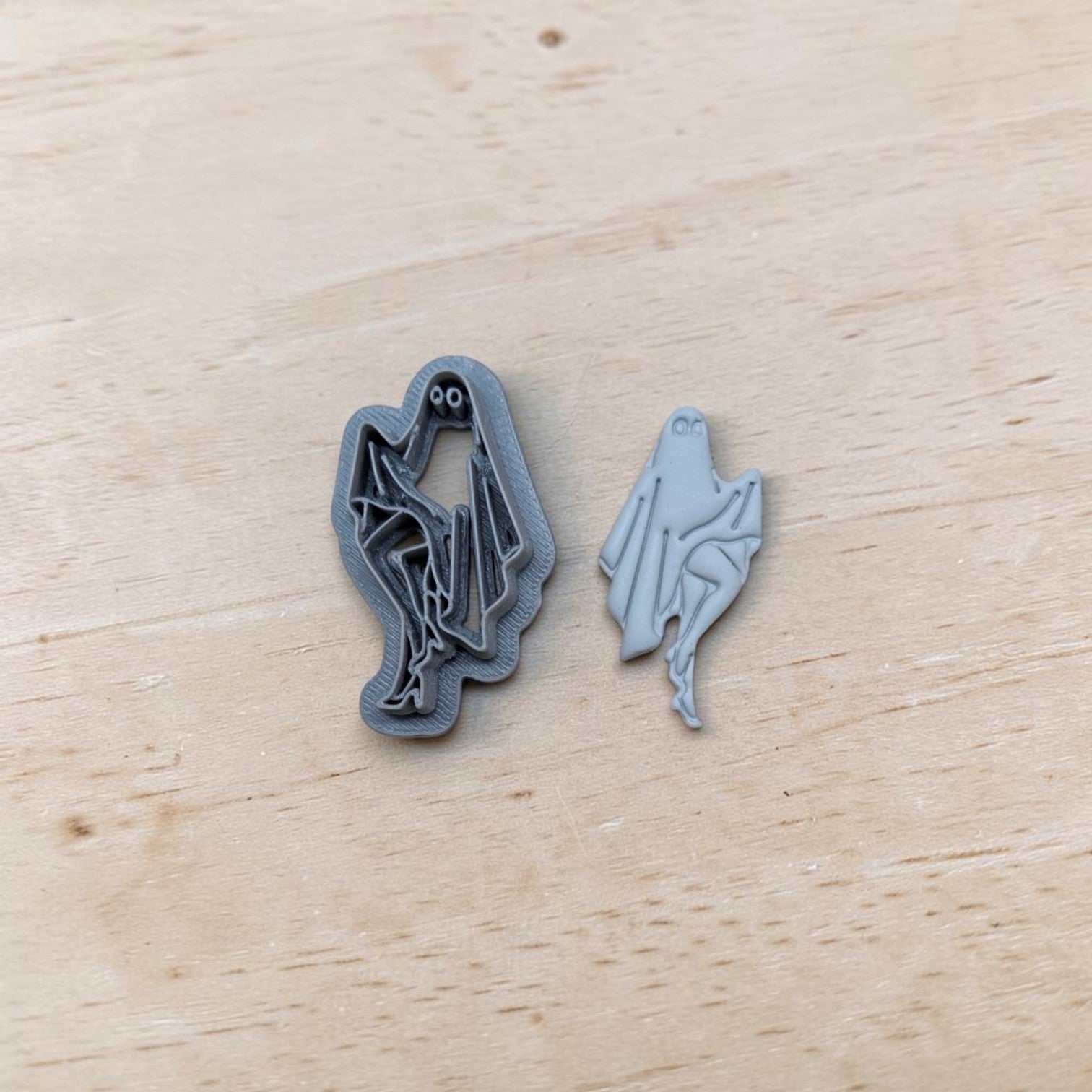 Two small ghost-shaped accessories, one dark gray and one light gray, displayed on a light wood surface.